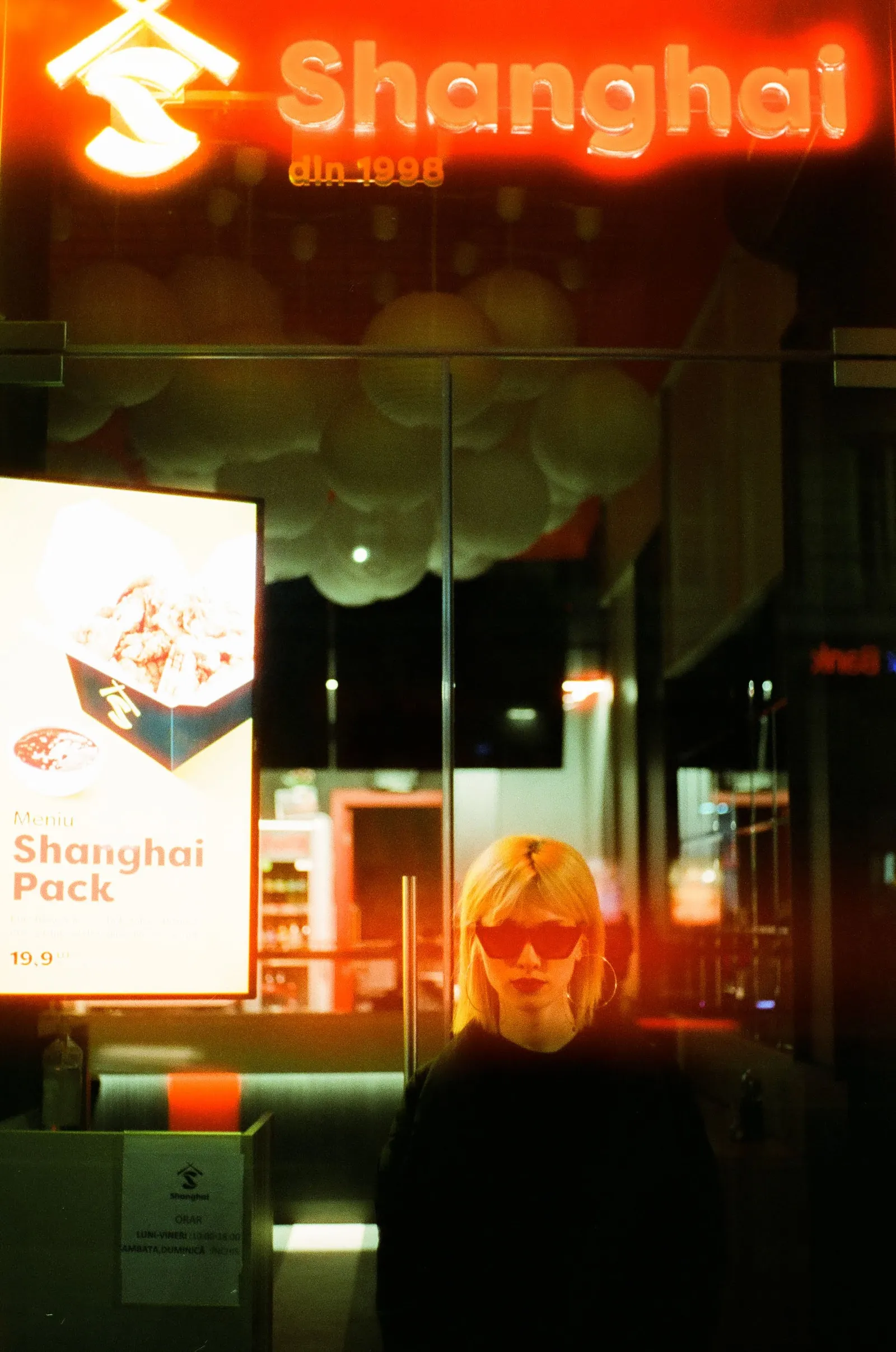 Oana in dark sunglasses outside the Shanghai takeaway, washed in red neon