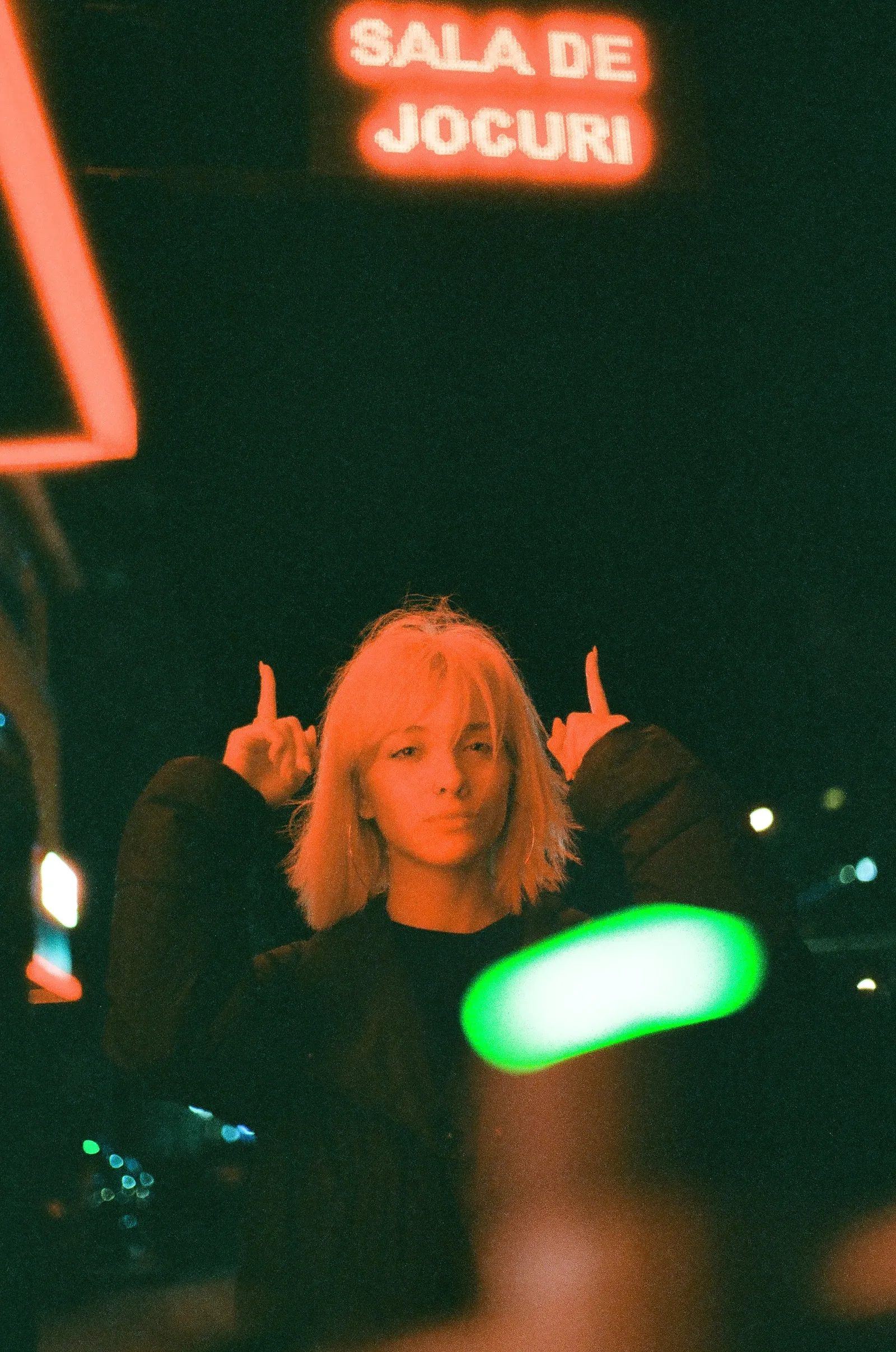 Oana pointing both index fingers upward beneath a red 'Sala de jocuri' sign