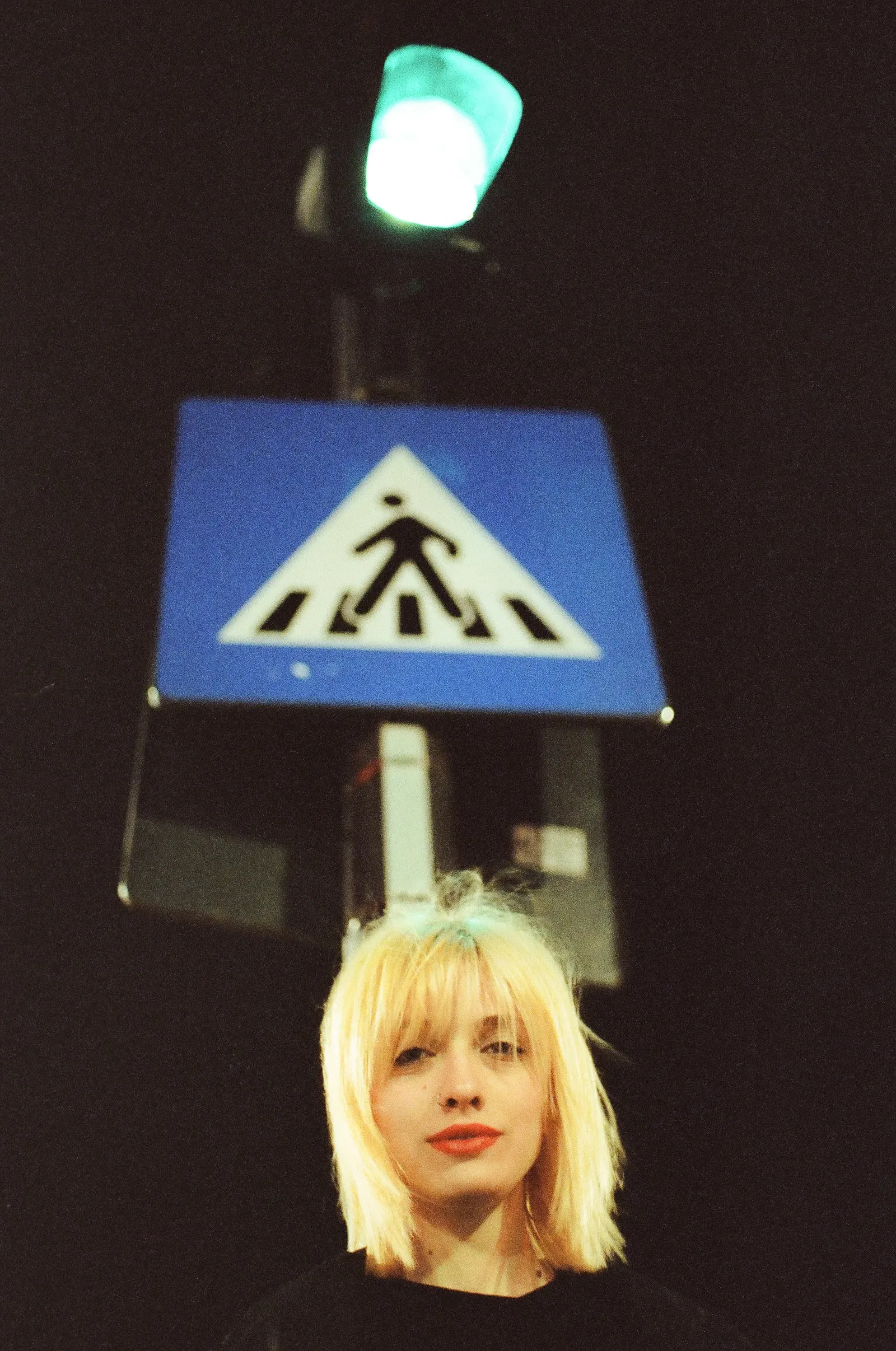 Oana looking up beneath a blue pedestrian-crossing sign and a green traffic light