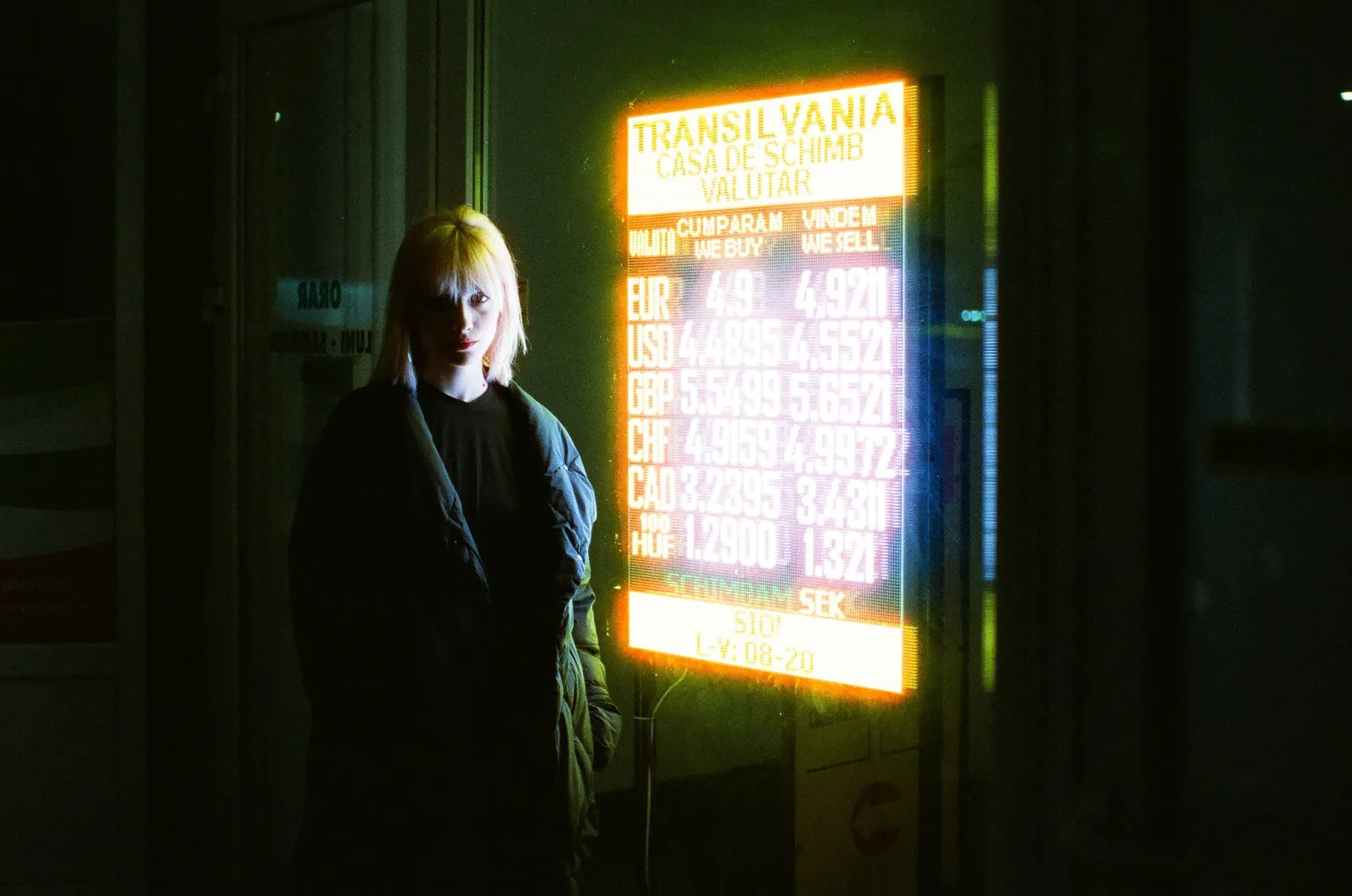 Oana beside the bright orange board of a Transilvania currency exchange
