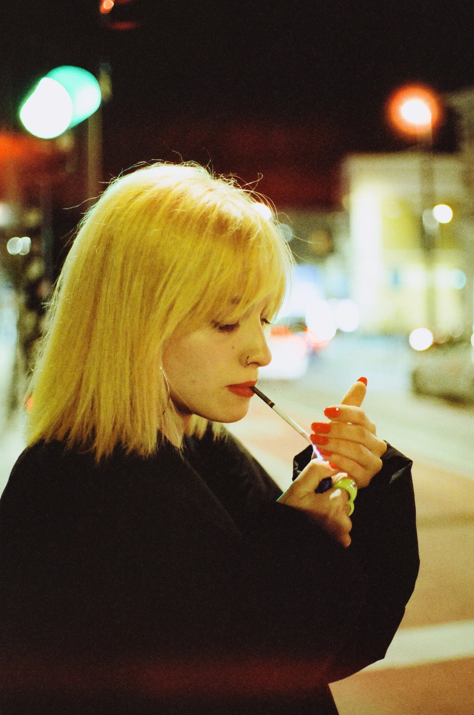 Oana in profile, lighting a cigarette, warm streetlight on blonde hair