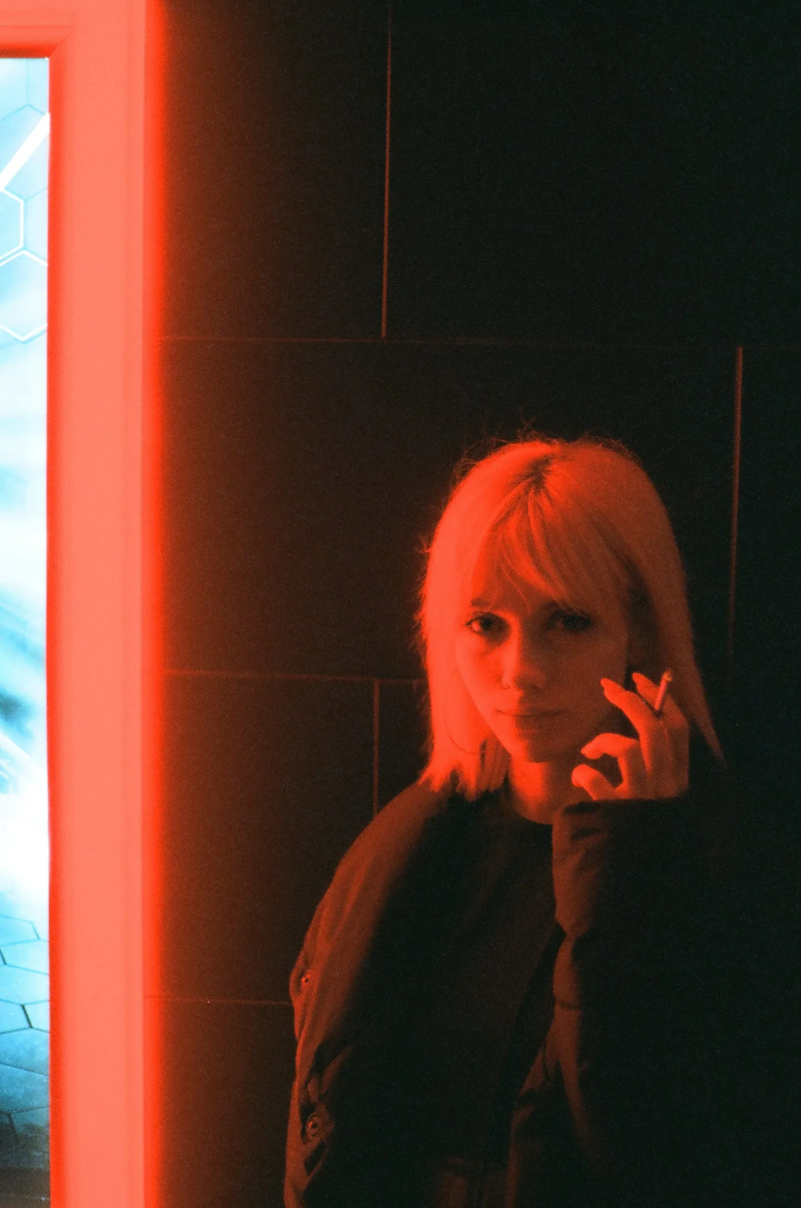 Oana half in shadow against a red-lit wall, hand raised near her face