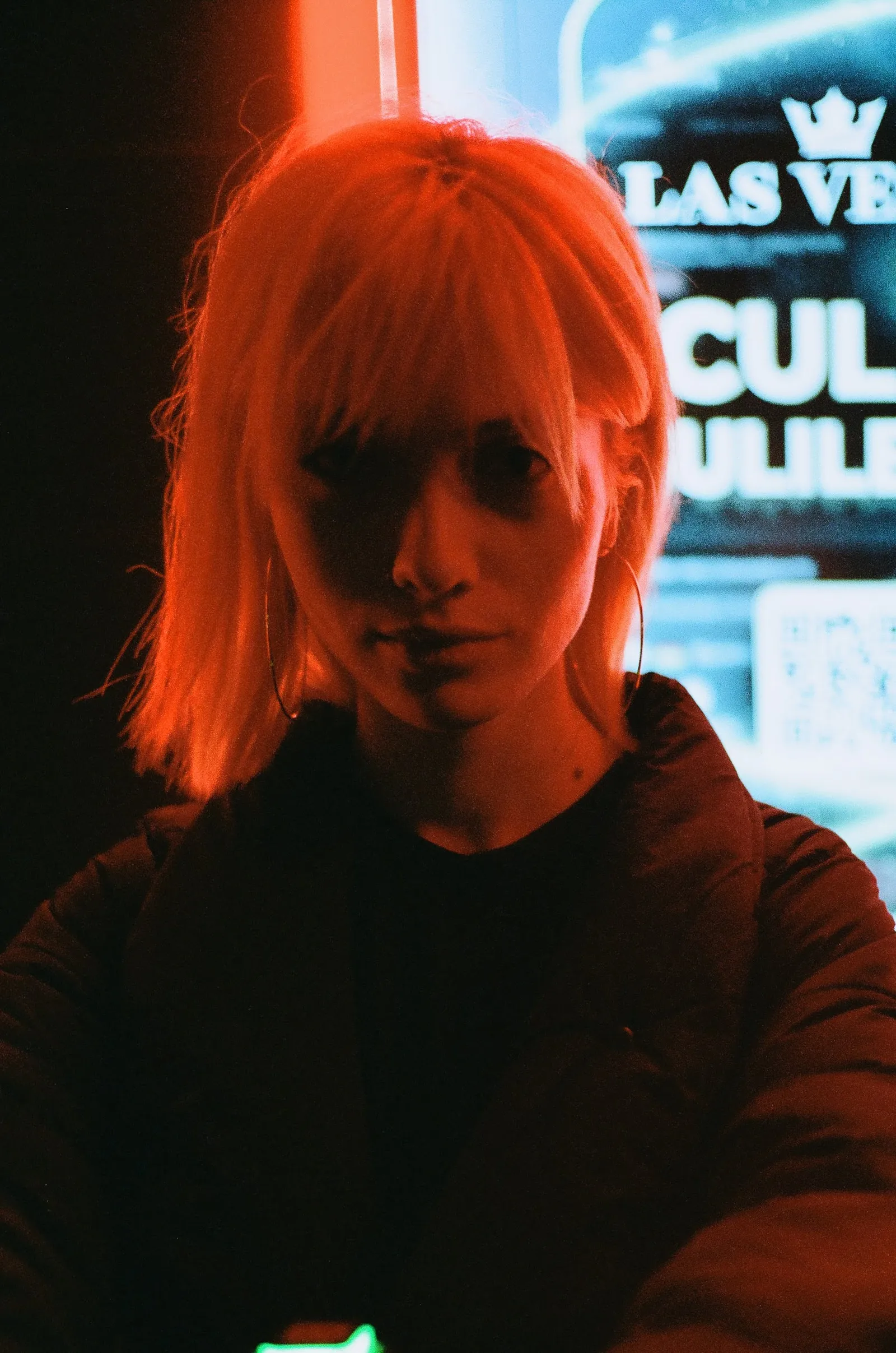 Tight portrait of Oana drenched in red light, neon signage glowing behind